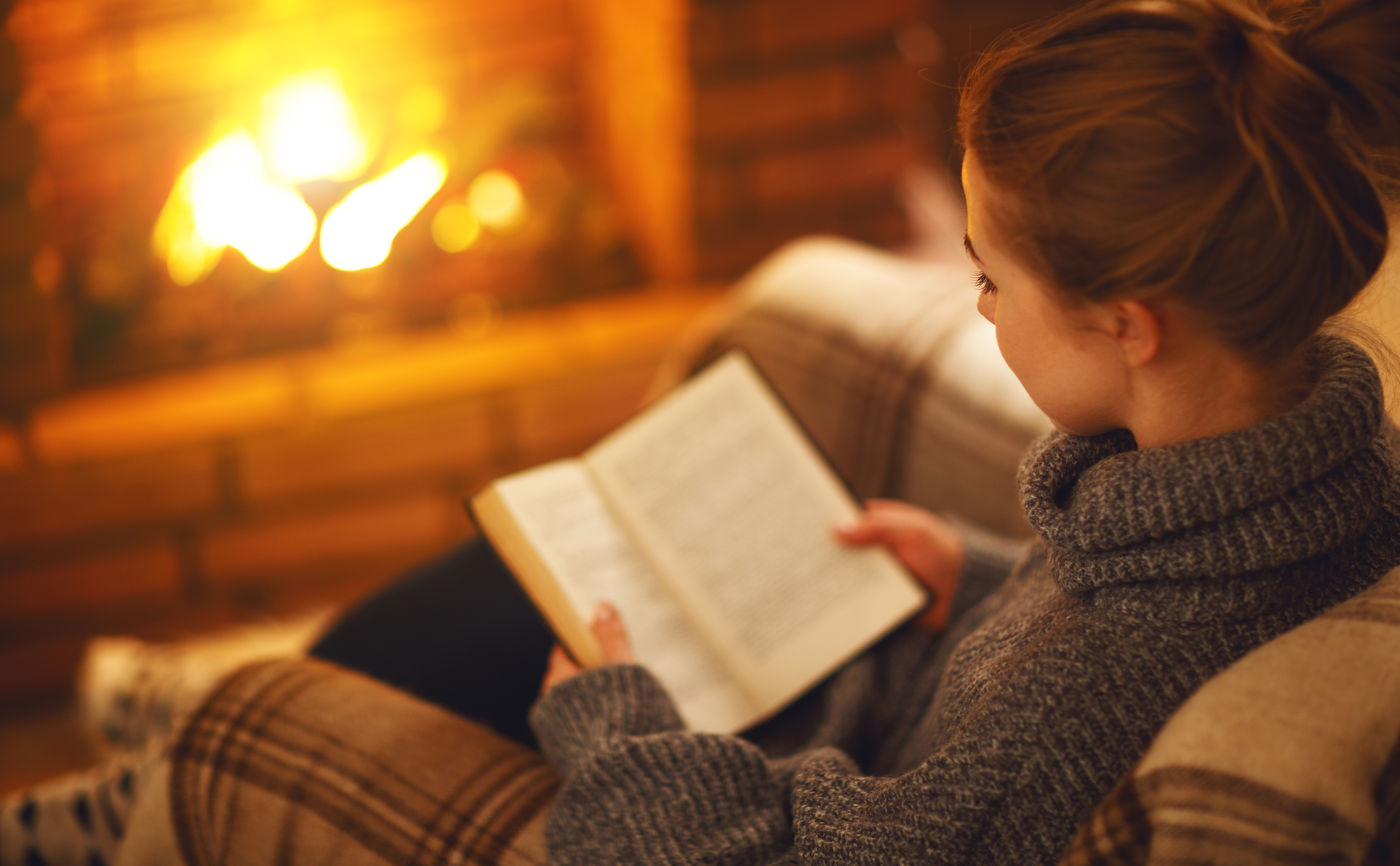 Person reading a book by a fireplace.